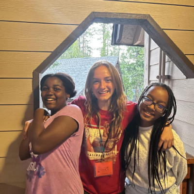 Three children posing and smiling in a cabin doorway.